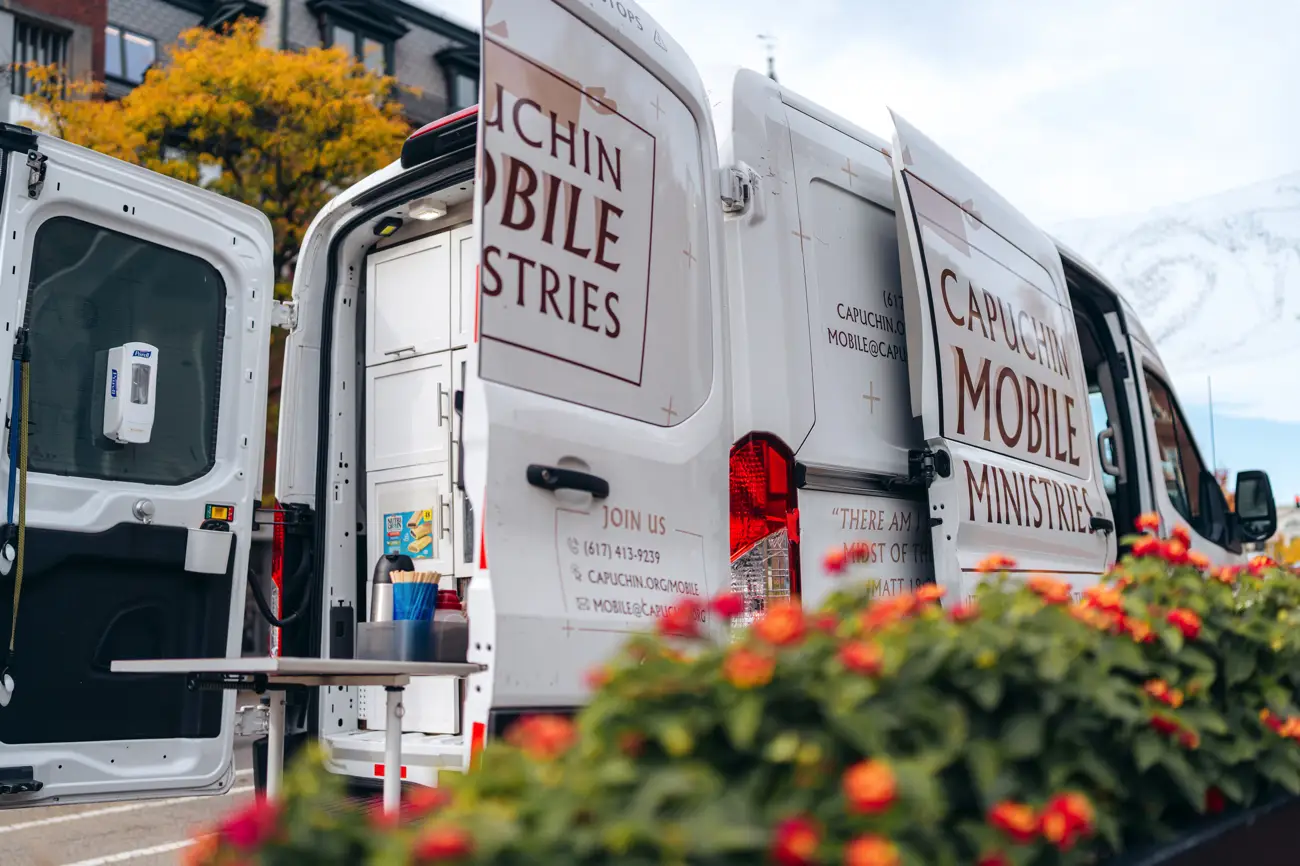 Open Capuchin Mobile Ministries van with supplies inside, surrounded by flowers and autumn trees.