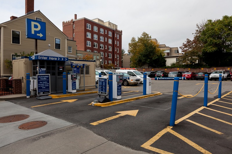 Municipal parking lot entrance with payment kiosks, an “Enter Here” sign, directional arrows, and marked spaces